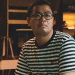 Indoor portrait of a man with glasses wearing a striped shirt, showcasing calm expression in Dalat, Vietnam.